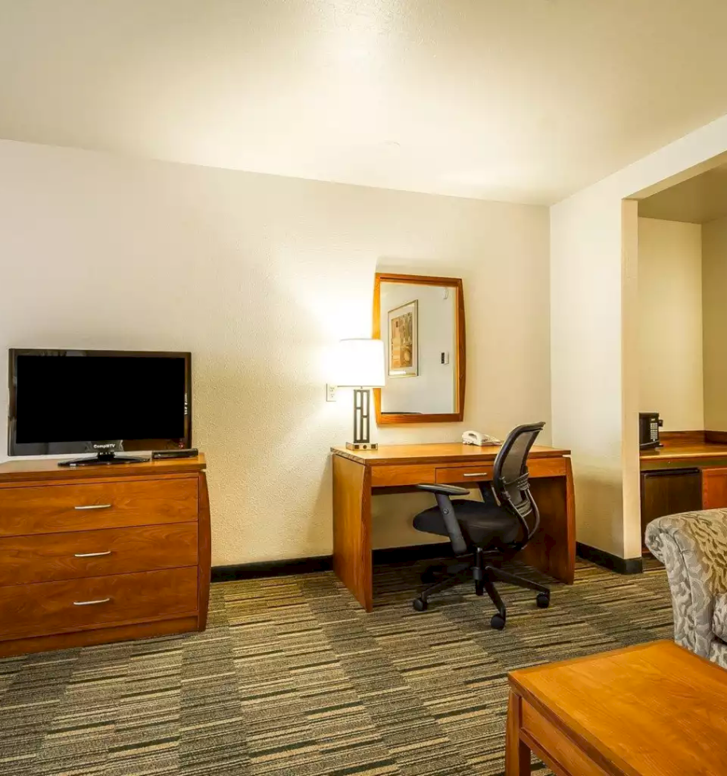 A tidy hotel room with a TV on a dresser, a desk with lamp and office chair, and part of a bed in view.