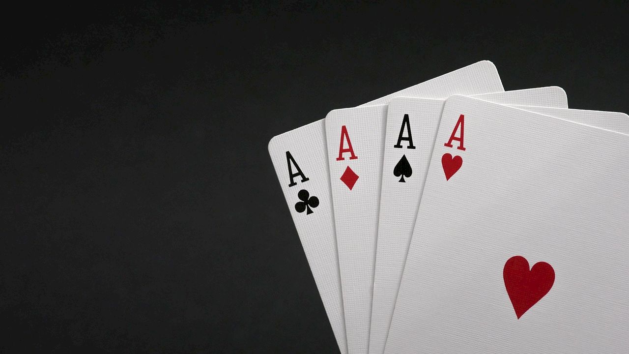A fan of playing cards showing four Aces (clubs, diamonds, spades, and hearts) on a dark background.